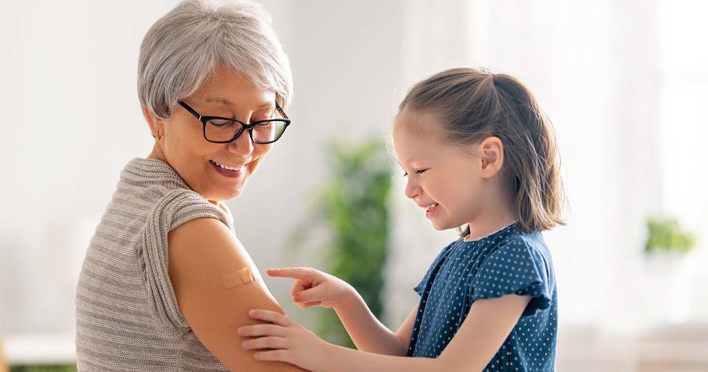 Grandmother with her grandchild looking at the bandaid from the vaccine she just got. They are both smiling and joyful.